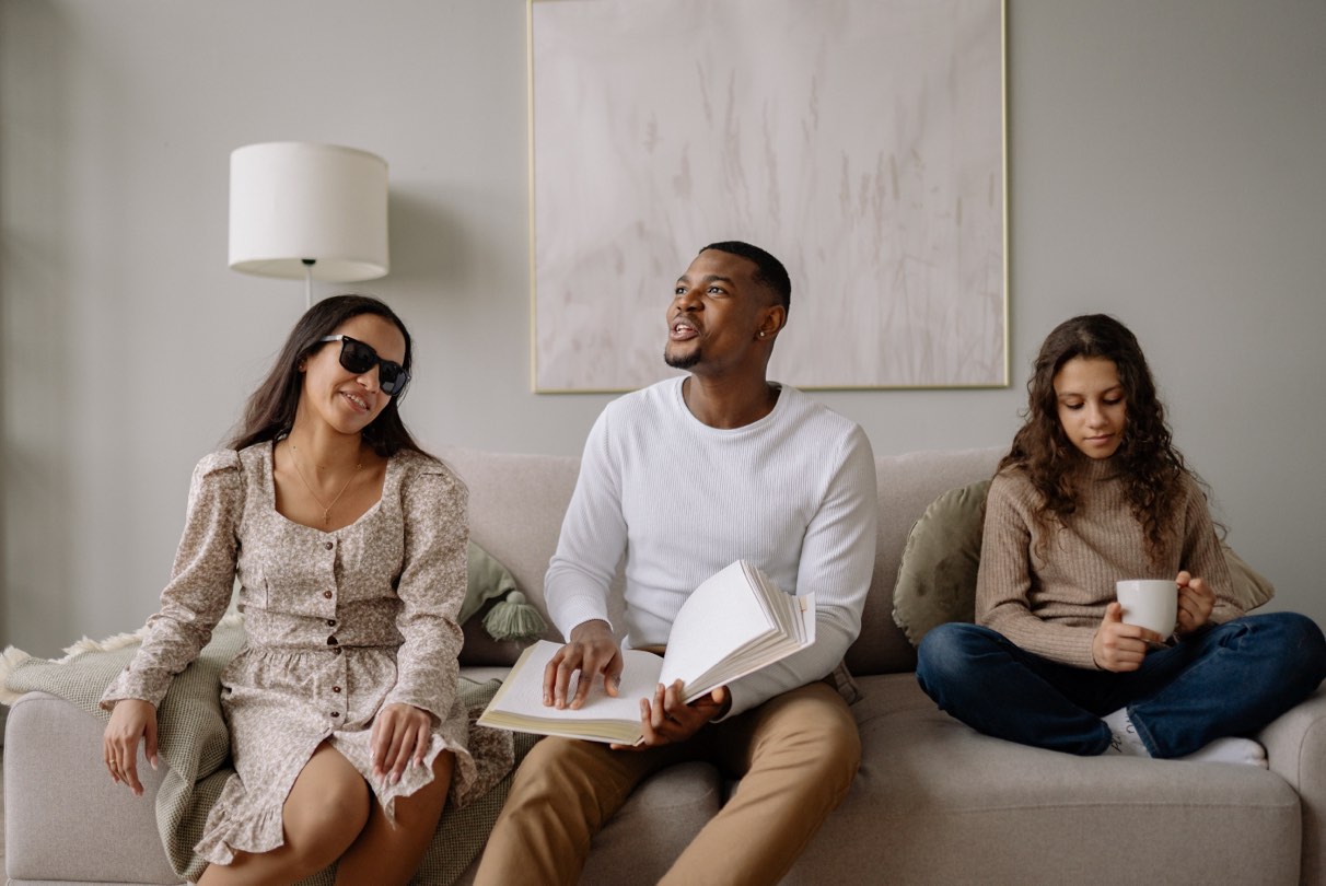 Two women and a man reading braille sitting on a couch