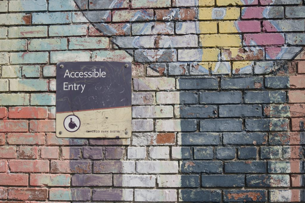 A sign saying Accessible Entry on a colourful brick wall