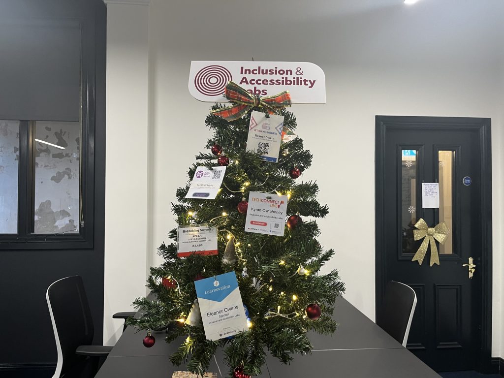 Christmas tree decorated with lights and ID's from tech conferences, and a sign with the IA Labs logo at the top of the tree