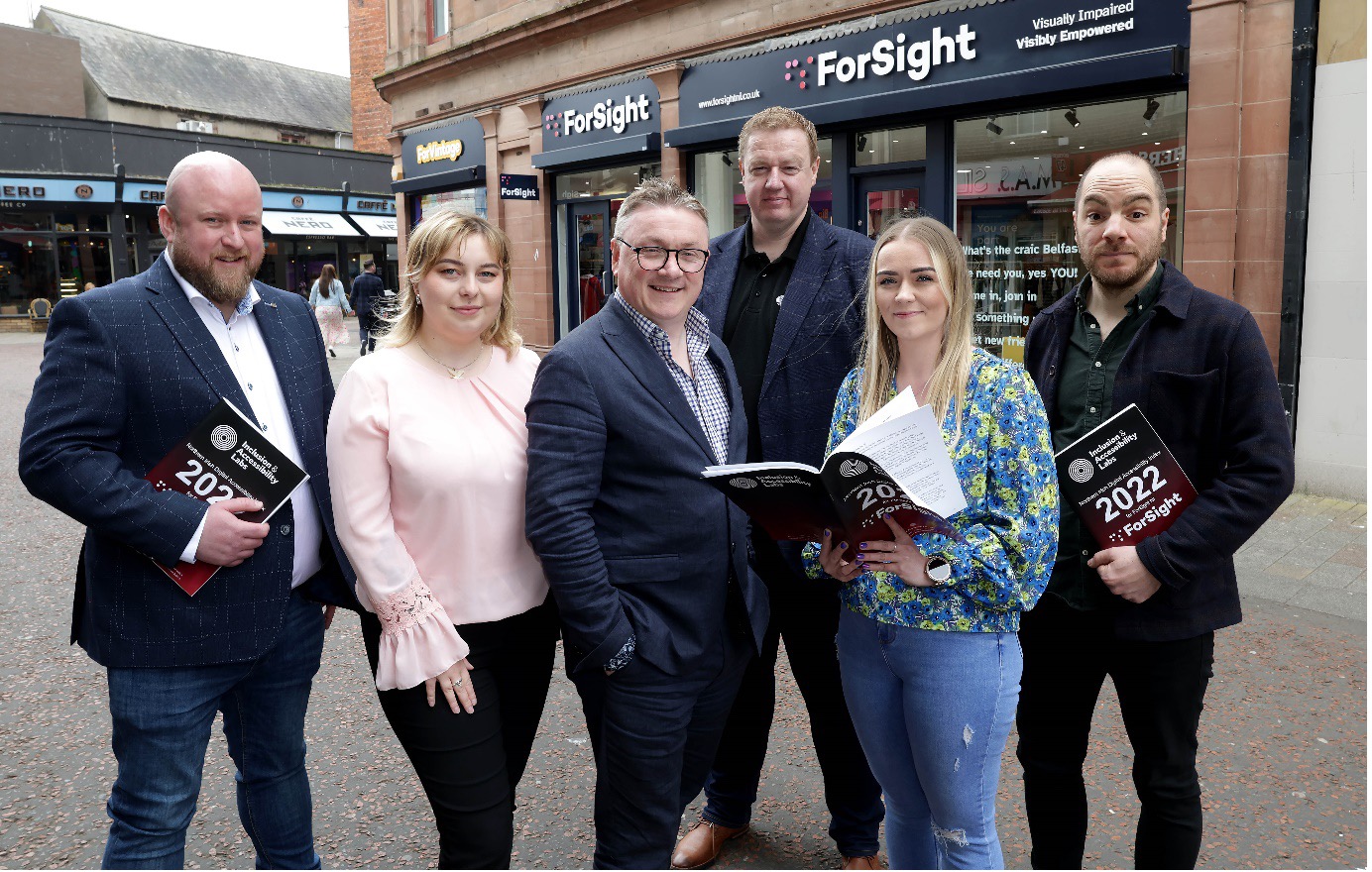 Sean Doran, Adela Buliman, Chris White. Kyran O'Mahoney, Amanda McClure, and Robbie Best holding the NI DAI Report in front of a ForSight shop.