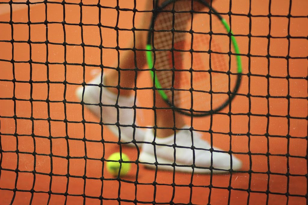 Tennis player holding a racket as they walk beside the net and a tennis ball