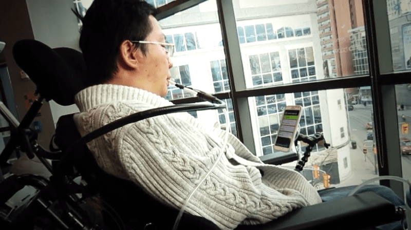 Person in a wheelchair using a sip and puff switch to interact with a mobile phone